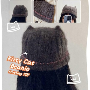 May include: A dark gray knitted beanie with cat ears and a pink stitched trim. The text "Kitty Cat Beanie Knitting PDF" is displayed in orange and white. The beanie is shown on a person's head, with close-up shots of the hat.