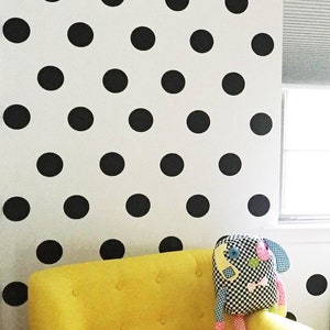 May include: A yellow armchair with a black and white polka dot wall behind it. A small black end table with a lamp sits next to the chair. A stuffed animal sits on the chair.