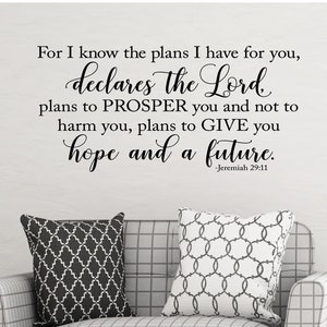May include: A black and white wall decal with a religious quote from Jeremiah 29:11. The quote reads "For I know the plans I have for you, declares the Lord, plans to PROSPER you and not to harm you, plans to GIVE you hope and a future." The quote is displayed on a white wall behind a gray couch with black and white patterned throw pillows.