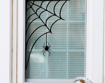 May include: Black spider web window cling with a spider hanging from the web. The web is in the corner of the window and the spider is hanging down in the middle of the window.