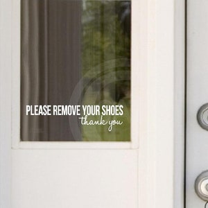 May include: White door with a glass panel featuring a sign that reads "Please remove your shoes, thank you". The door has a silver door knob and a silver deadbolt.