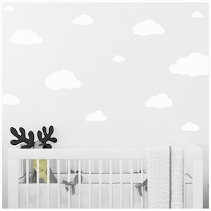 May include: White crib with a white blanket and a yellow stuffed animal. The wall behind the crib is painted white and has white cloud decals.