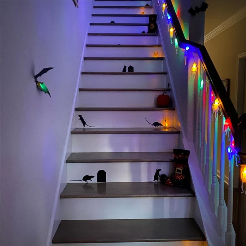 May include: A white staircase decorated with black silhouettes of rats and bats, and colourful fairy lights for Halloween.