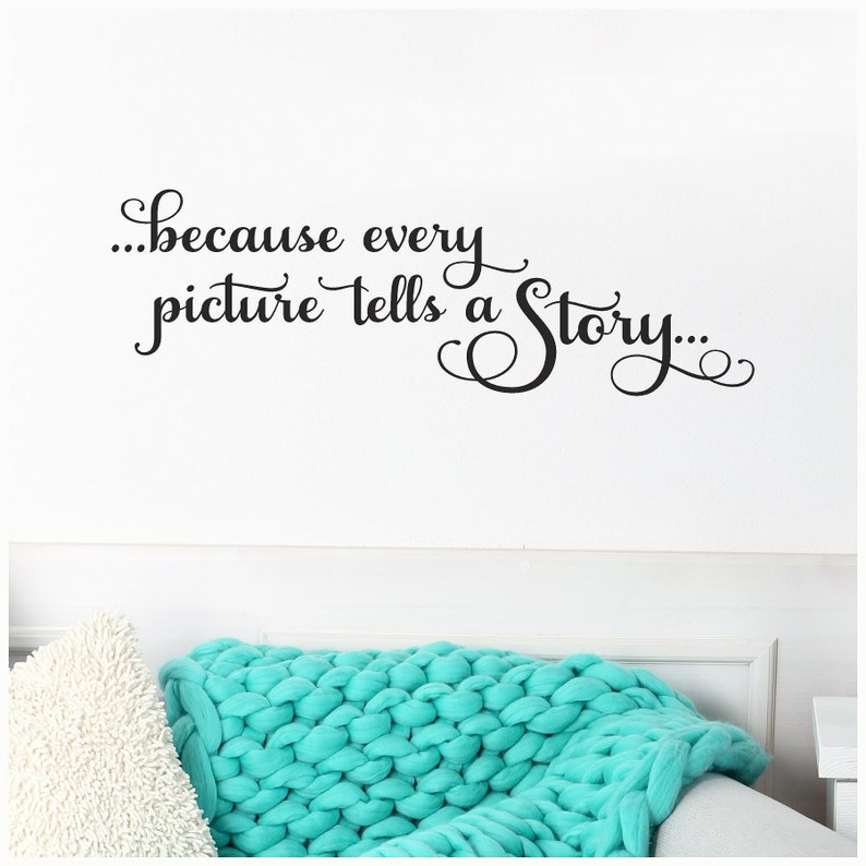 May include: A white wall with the quote "...because every picture tells a Story..." in black script. Below the quote is a white pillow and a turquoise chunky knit blanket.