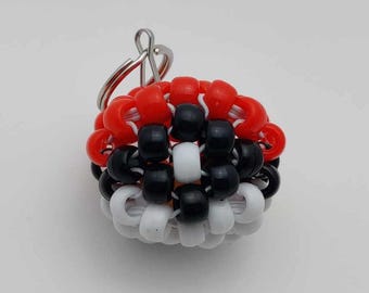 May include: A red, black, and white beaded keychain with a silver key ring. The beads are arranged in a pattern resembling a Pokeball.