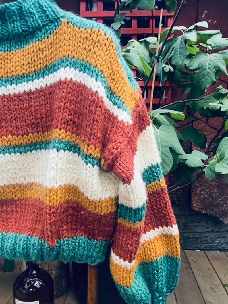Pu&ograve; includere: Un maglione di lana grossa con un motivo a righe in tonalit&agrave; turchese, bianco, giallo senape e ruggine.