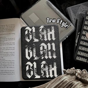 May include: A black e-reader case featuring the repeated white text "BLAH BLAH BLAH" in a gothic font style. The case is positioned on an open book page. A translucent gray protective cover with the text "New Style!" is visible nearby.