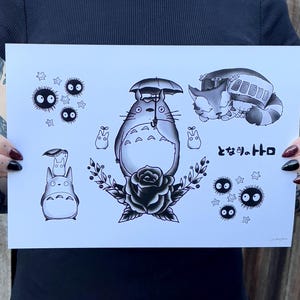Puede incluir: Una impresión en blanco y negro con una colección de ilustraciones de personajes de la película animada "Mi vecino Totoro". La impresión incluye a Totoro sosteniendo un paraguas, un autobús gato durmiendo y varios espíritus de hollín. El texto japonés "となりのトトロ" está incluido en la impresión.