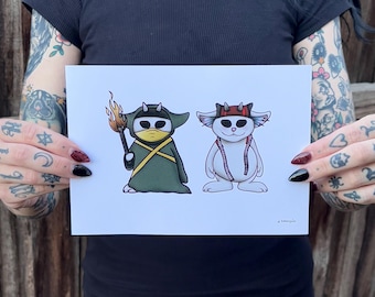 May include: A white print with two cartoon characters. The character on the left is green and wearing a yellow mask. The character on the right is white and wearing a red hat. The print has the text "a bobbysue" in the bottom right corner.