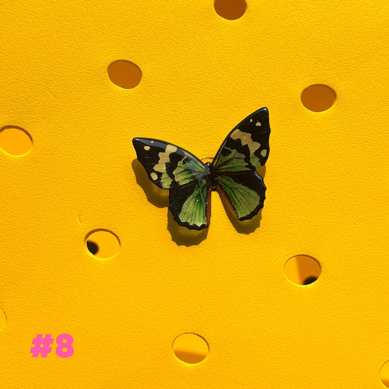 May include: A butterfly-shaped accessory with green and gold details, set against a bright yellow background with circular cutouts. The accessory has a detailed wing pattern and is likely a decorative item. The number "#8" is printed in pink in the lower left corner.