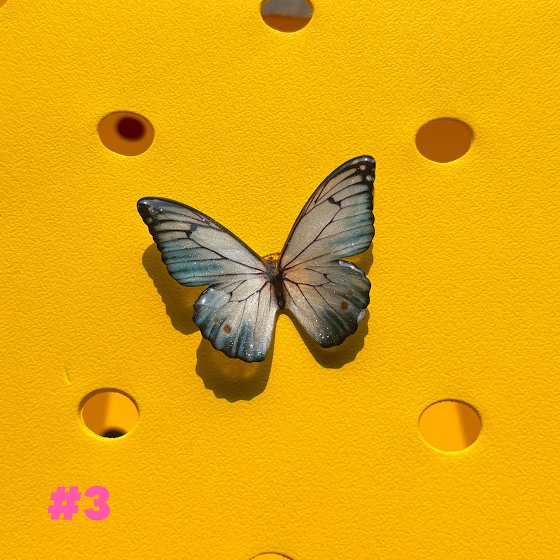 May include: A decorative butterfly with blue and white wings, set against a bright yellow background. The butterfly has intricate details and is positioned in the center. The number "#3" is displayed in pink in the lower left corner.