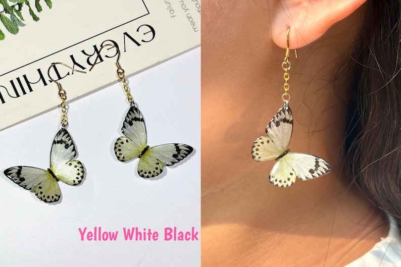 K&ouml;nnte beinhalten: Ohrringe mit Schmetterlingsanh&auml;ngern in Gelb, Wei&szlig; und Schwarz. Die Ohrringe haben eine goldfarbene Kette und einen Haken. Die Schmetterlingsfl&uuml;gel haben schwarze Punkte und Aderdetails. Der Text "Yellow White Black" ist ebenfalls im Bild enthalten.