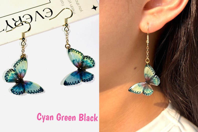 K&ouml;nnte beinhalten: Ohrringe mit Schmetterlingen in Cyan, Gr&uuml;n und Schwarz. Die Ohrringe haben eine goldfarbene Kette und einen Haken. Die Schmetterlingsfl&uuml;gel haben ein detailliertes Muster und sind an einer goldfarbenen Kette befestigt.