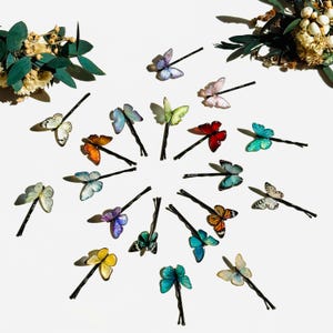 May include: A collection of hair pins featuring miniature butterfly ornaments in a variety of vibrant colors including blue, orange, yellow, green, and red. Each butterfly is attached to a thin black metal bobby pin arranged in a circular pattern.