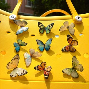 May include: A bright yellow tote bag adorned with a collection of colorful butterfly charms. The butterflies feature various patterns and shades, including blue, orange, green, and cream, creating a vibrant and eye-catching design. The bag has two yellow handles.