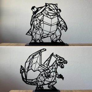 Könnte beinhalten: Zwei schwarze geometrische Skulpturen von Pokémon-Charakteren, einem schildkrötenartigen Wesen und einem Drachen, werden auf einer Holzoberfläche gezeigt. Die Skulpturen bestehen aus miteinander verbundenen Linien, wodurch ein Low-Poly-Effekt entsteht. Jede Skulptur ist auf einem schwarzen Sockel montiert.