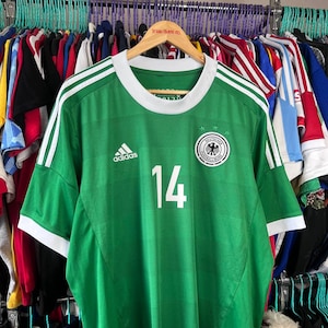 May include: A green football shirt with white trim on the collar and sleeves. The jersey features the white Adidas logo on the right chest, the number 14 in white in the centre, and the Deutscher Fussball-Bund crest on the left chest with three stars.