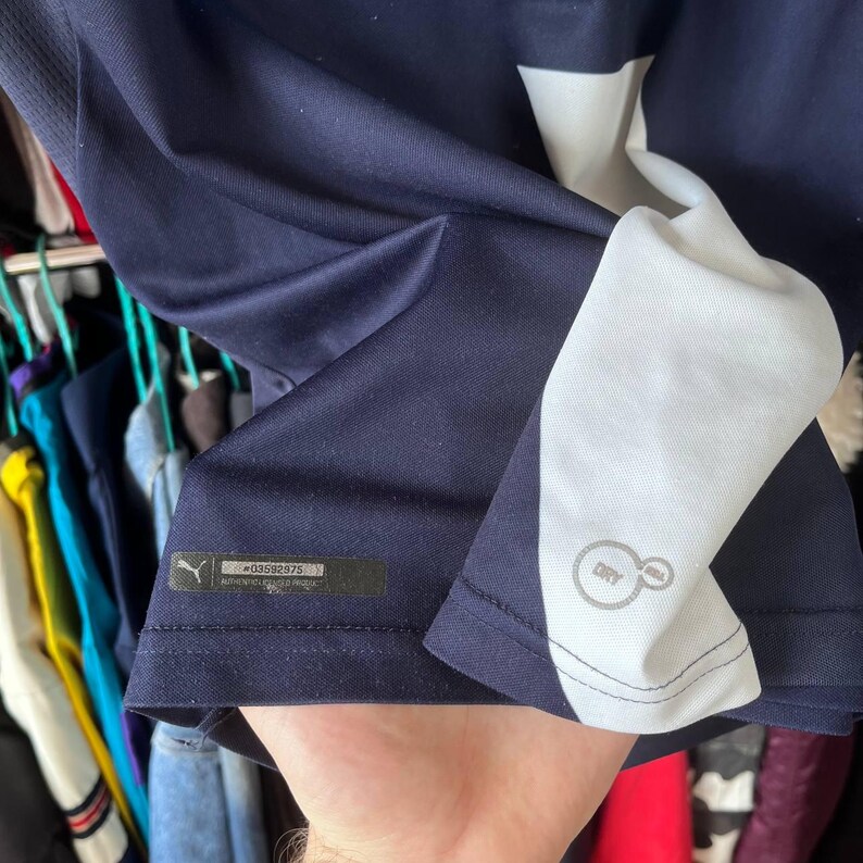 Pu&ograve; includere: Maglia sportiva blu navy con dettagli bianchi. La maglia presenta un pannello bianco sul lato e il logo Puma. La maglia ha un'etichetta con il testo "#G3592975 AUTHENTIC LICENSED PRODUCT". La maglia ha anche il logo "DRY CELL".