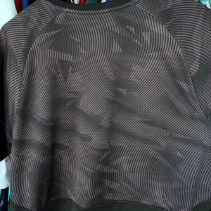 Puede incluir: Una camiseta negra de manga corta con un patr&oacute;n abstracto gris oscuro de l&iacute;neas diagonales, onduladas y entrecruzadas. La prenda tiene un cuello redondo negro s&oacute;lido y una banda horizontal negra s&oacute;lida a lo largo del dobladillo inferior.