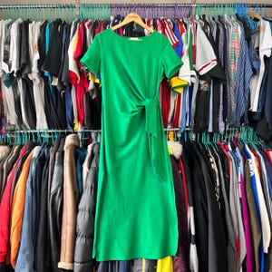 May include: A vibrant green midi dress featuring short sleeves, a round neckline, and a side-tie detail at the waist that creates soft, gathered folds across the front of the garment. The dress has a straight, clean silhouette and hemline.