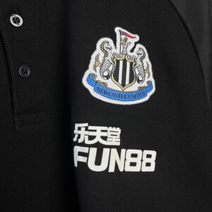 May include: Black polo shirt featuring the Newcastle United crest on the chest. The crest includes two seahorses, a shield, and the words "Newcastle United". Below the crest are Chinese characters and the word "FUN88".