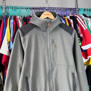 May include: A gray hooded jacket with a full-length zipper and a small chest pocket. The jacket has black shoulder accents and a brown zipper pull. The jacket is hanging on a wooden hanger with the text "POLAR SKATE CO."