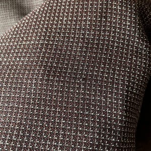 May include: Close-up of a textured fabric with a repeating pattern of small white dots on a dark brown background. The fabric appears to be woven, with a subtle sheen. The overall effect is a sophisticated, geometric design.