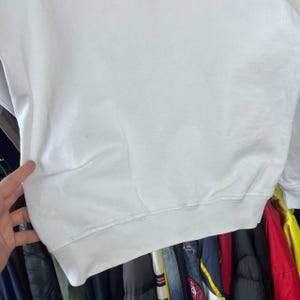 May include: A white sweatshirt with a crew neck and long sleeves. The bottom hem and cuffs are ribbed. The garment is made of a soft, comfortable material. The sweatshirt is a casual, everyday wear item.