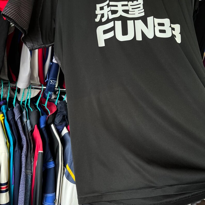 Puede incluir: Una camiseta deportiva negra de manga corta con texto blanco que dice "乐天堂" sobre la palabra "FUN88" impresa en una fuente negrita sin remates en el pecho. La prenda tiene una textura de tela suave y ligera y un cuello redondo simple.