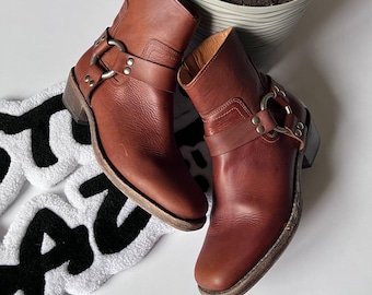 May include: A pair of brown leather ankle boots with buckles and straps. The boots have a pointed toe and a low heel.