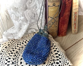 May include: A blue beaded drawstring bag with a crocheted design. The bag is hanging from a cord and is resting on a white crocheted doily.