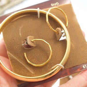 May include: Gold-toned jewelry set with a bangle bracelet and two pairs of hoop earrings. The set is displayed on a brown velvet background with the word "DUO" and the price "$5.97" printed on the packaging.