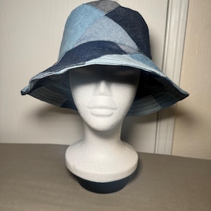 May include: A bucket hat constructed from various shades of blue denim fabric, featuring a patchwork design with triangular and geometric panels in light, medium, and dark indigo tones. The hat has a wide, downward-sloping brim and a rounded crown.