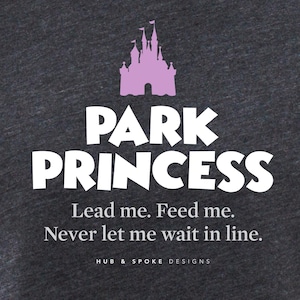 May include: Dark grey heather t-shirt with a white graphic of a pink castle and the text "PARK PRINCESS". The text below the graphic reads "Lead me. Feed me. Never let me wait in line." and "HUB & SPOKE DESIGNS".