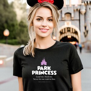 Może przedstawiać: Czarny t-shirt z r&oacute;żowym nadrukiem zamku i tekstem "Park Princess. Lead me. Feed me. Never let me wait in line."