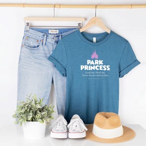 Może przedstawiać: Koszulka w kolorze niebiesko-zielonym z nadrukiem r&oacute;żowego zamku i tekstem "Park Princess Lead me. Feed me. Never let me wait in line."