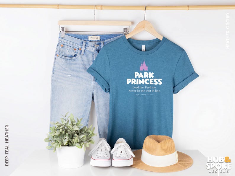 Może przedstawiać: Koszulka w kolorze niebiesko-zielonym z nadrukiem r&oacute;żowego zamku i tekstem "Park Princess Lead me. Feed me. Never let me wait in line."
