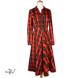 May include: A long-sleeved red, black, and gold plaid dress with a collared neckline and button-down front. The dress is displayed on a mannequin and has a flared skirt. The brand logo "Hey Viv!" is visible in the lower left corner.
