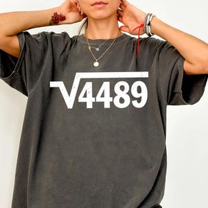 May include: Dark gray t-shirt with the white text "√4489" in a square root symbol. The shirt has short sleeves and a relaxed fit. The shirt is made of a soft, comfortable material.