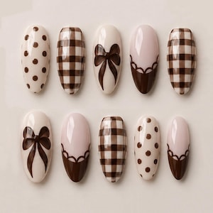 May include: A set of ten almond-shaped press-on nails featuring a cohesive brown and cream color palette. The designs include dark brown polka dots on a cream base, a brown and cream checkered pattern, solid brown bows, and scalloped brown tips.