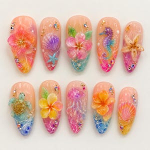 May include: A set of ten almond-shaped press-on nails featuring a gradient base with 3D embellishments including pink and orange hibiscus flowers, a purple seashell, a blue starfish, a seahorse, a sea turtle, a jellyfish, and rhinestones.