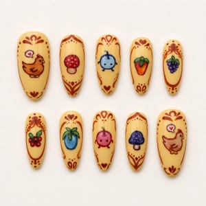 May include: A collection of ten almond-shaped false nails with a cream base. Each nail is hand-painted with a different design, such as a chicken, mushroom, blueberry, strawberry, and grapes. The designs are framed with brown decorative patterns.