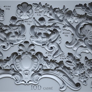 May include: A gray silicone mold featuring various ornate, baroque-style decorative elements. Designs include floral patterns, cherubs, and scrollwork, with measurements in milliliters and grams. The text "IOD CADRÉ" is visible.