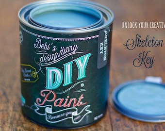 May include: A teal blue paint can with a black label that says "Debi's design diary DIY Paint Because you can" and "Skeleton Key". The can is open and the lid is sitting next to it. The text "Unlock Your Creativity Skeleton Key" is written in black on a white background.