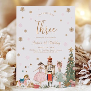 May include: A white and gold Christmas-themed birthday invitation with a pink snowflake design. The invitation says "Oh Christmas Three" and "Andin's 3rd Birthday". The invitation also includes a picture of a Nutcracker, a ballerina, and a Christmas tree.