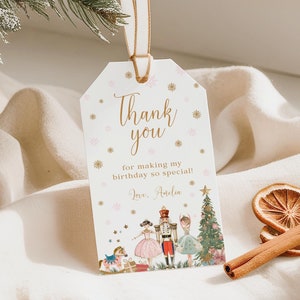 Könnte beinhalten: Weißer Dankeschön-Anhänger mit goldenen Glitzer-Schneeflocken und dem Text "Danke, dass du meinen Geburtstag so besonders gemacht hast! Liebe, Amelia". Der Anhänger zeigt eine Illustration zum Thema Nussknacker mit einem Mädchen in einem rosa Kleid, einem Nussknacker-Soldaten und einem Weihnachtsbaum.