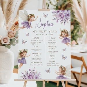 Könnte beinhalten: Ein helles Schild auf einer Staffelei mit dem Namen "Sophia" in Schreibschrift. Das Schild hat ein Feen-Thema mit Illustrationen von Feen, Schmetterlingen und floralen Akzenten in Lila. Der Text enthält "My First Year" und Statistiken.