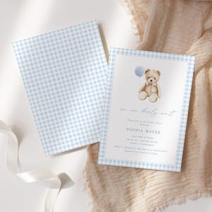Peut inclure: Une invitation de f&ecirc;te pr&eacute;natale bleu et blanc &agrave; carreaux vichy avec une illustration aquarelle d'un ours en peluche tenant un ballon bleu. Le texte sur l'invitation est "we can barely wait" et "Sophia Mayer".