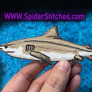 May include: An embroidered shark patch in brown and white with white stitching. The patch is on a blue background. WWW.SpiderStitches.com
