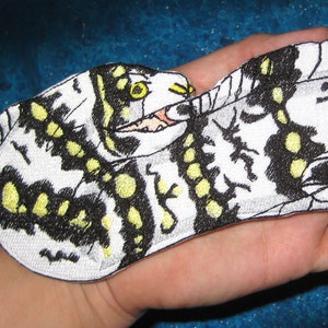 Könnte beinhalten: Ein weißer, schwarzer und gelber gestickter Aufnäher eines Schmetterlings mit ausgebreiteten Flügeln.